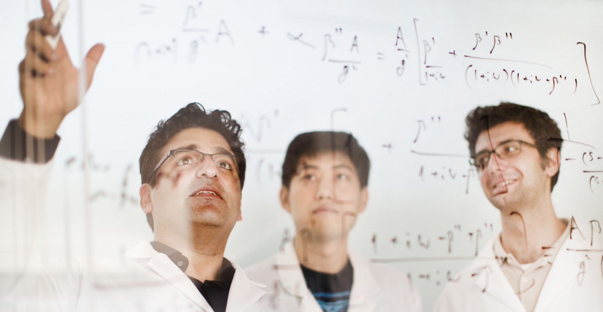 Instructor assists two students and points to calculations on the board