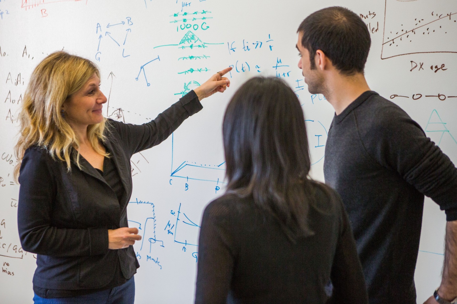 Instructor assists two students and points to calculations on the board 